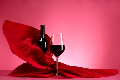 Stylish presentation of delicious red wine in bottle and glass on pink background. Space for text