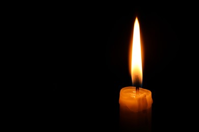 Photo of Burning candle on black background, closeup. Space for text