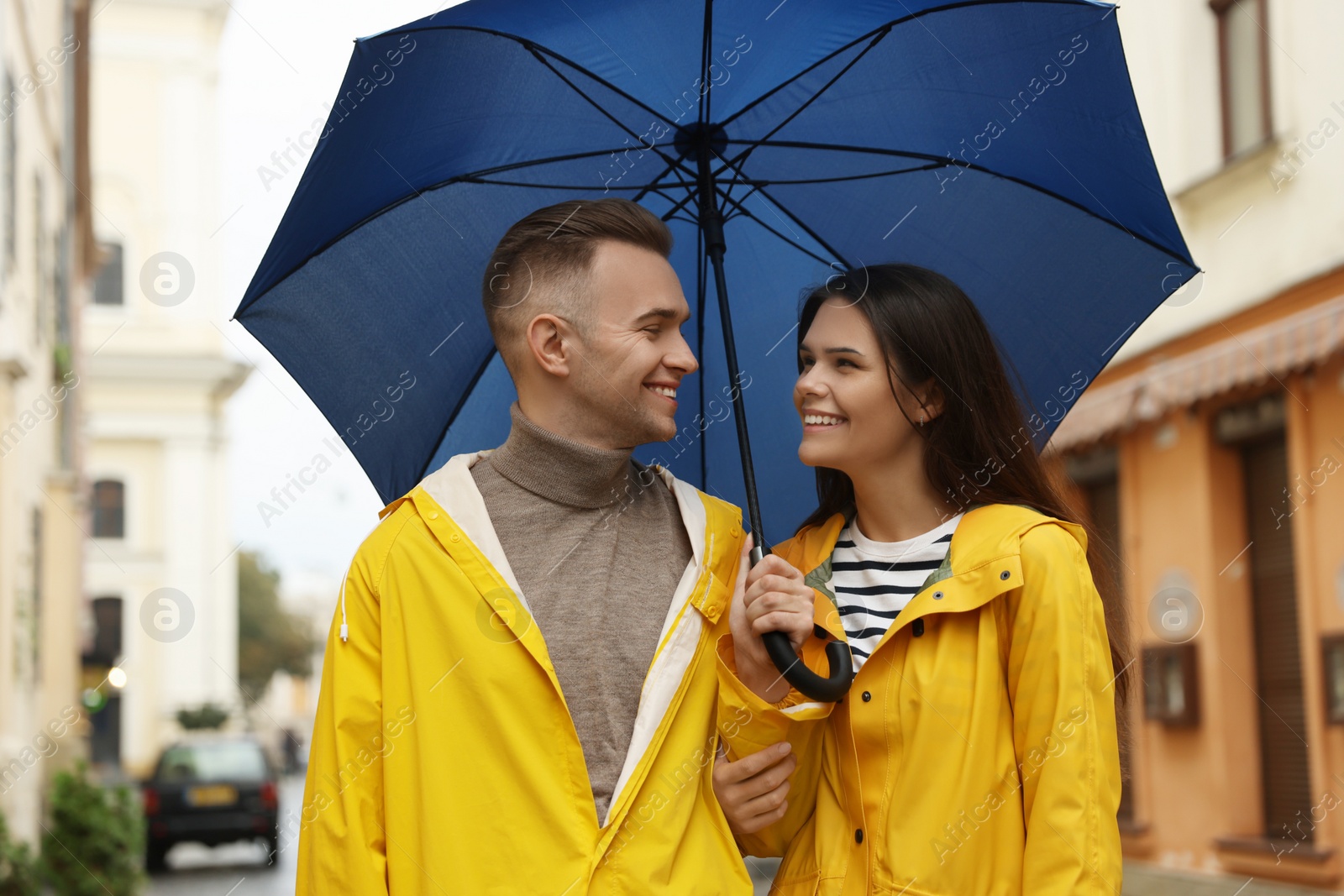 Photo of Lovely young couple with umbrella walking under rain on city street