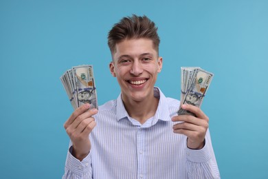 Photo of Happy man with dollar banknotes on light blue background