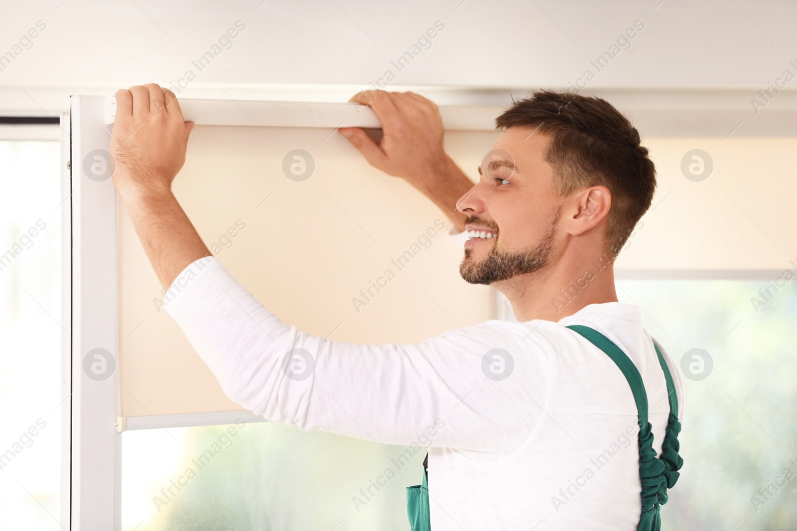 Image of Man in uniform installing roller window blind indoors