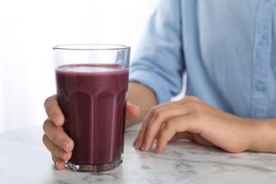 Photo of Woman with glass of fresh acai drink at white marble table, closeup