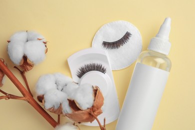 Photo of Bottle of makeup remover, cotton flowers, pad and false eyelashes on yellow background, flat lay