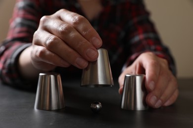 Photo of Woman playing thimblerig game with cups and metal ball at black table, closeup