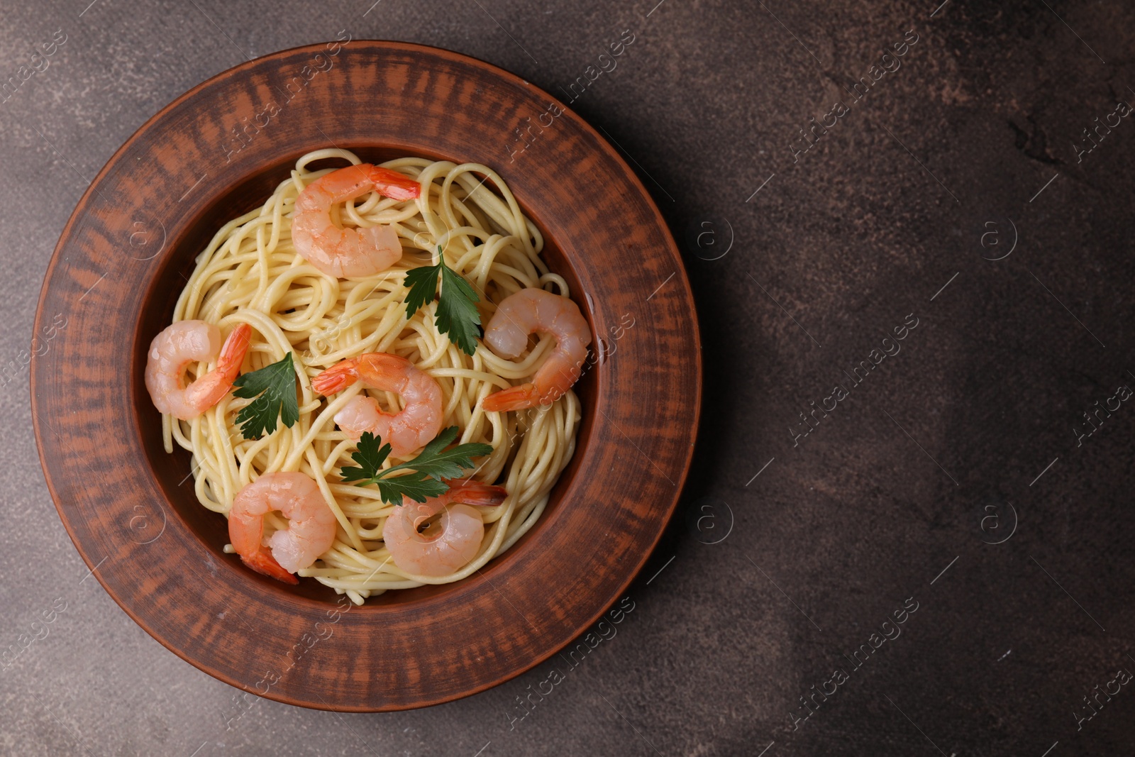 Photo of Tasty spaghetti with shrimps and parsley on brown textured table, top view. Space for text