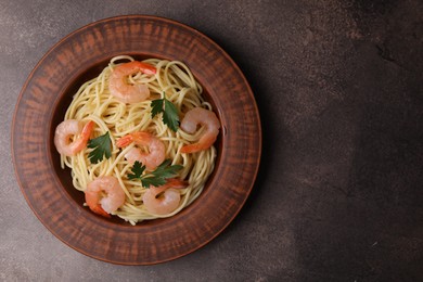 Photo of Tasty spaghetti with shrimps and parsley on brown textured table, top view. Space for text