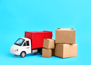 Photo of Truck model and carton boxes on light blue background. Courier service