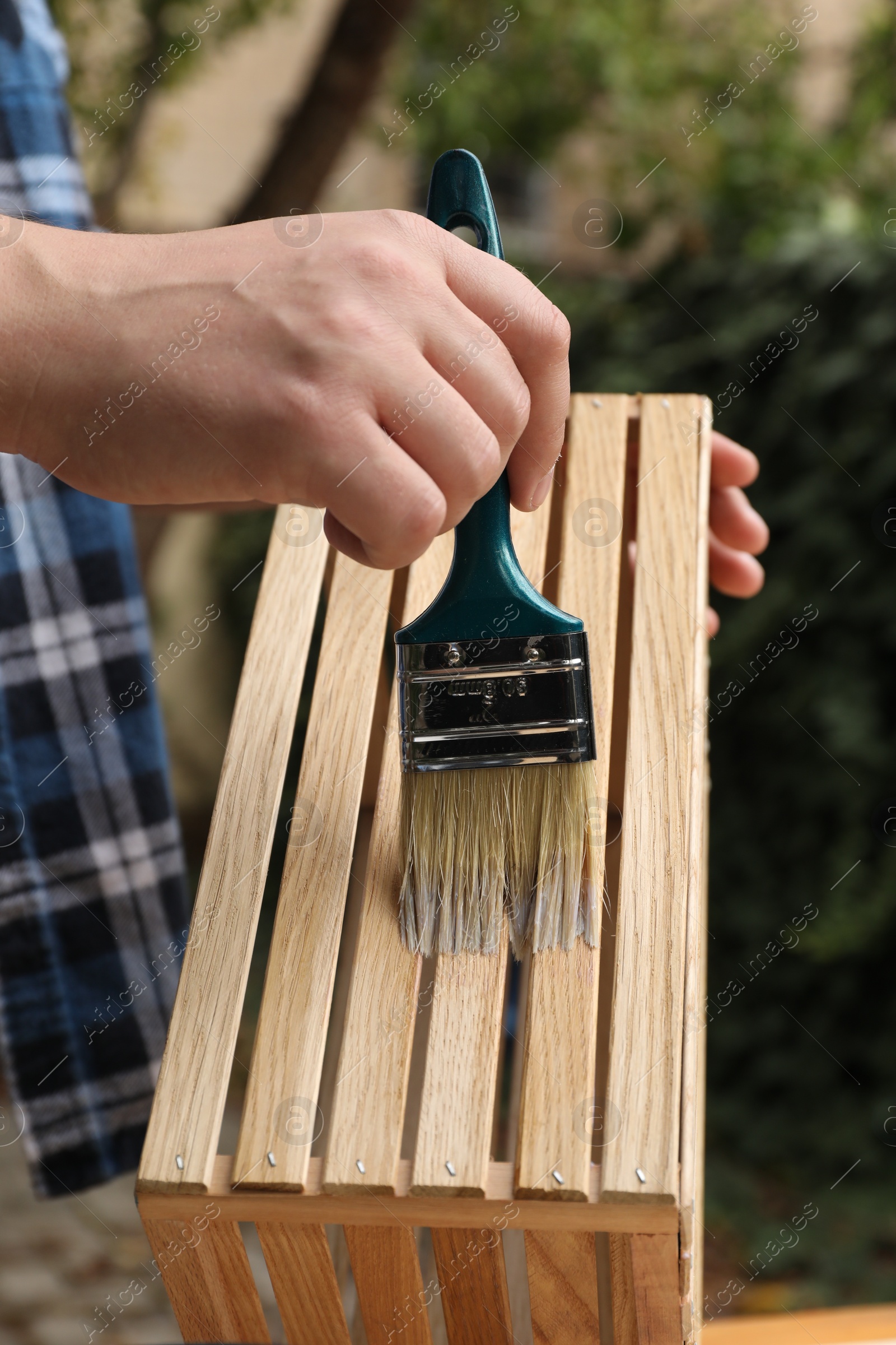 Photo of Man applying varnish onto wooden crate against blurred background, closeup