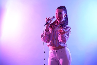 Photo of Emotional woman with microphone singing on bright background. Space for text