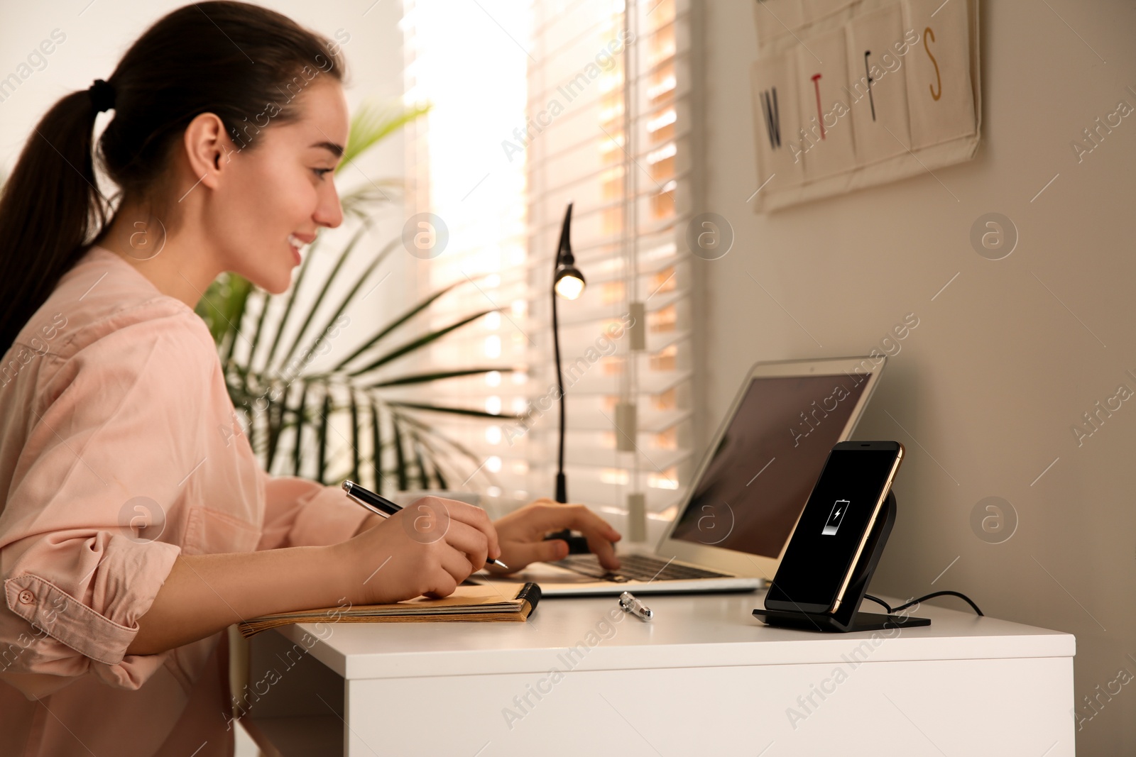 Photo of Woman working at table while her mobile phone charging with wireless device