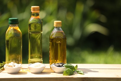 Photo of Different cooking oils and ingredients on wooden table against blurred green background. Space for text