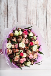 Photo of Beautiful bouquet of flowers and chocolate candies on white wooden table