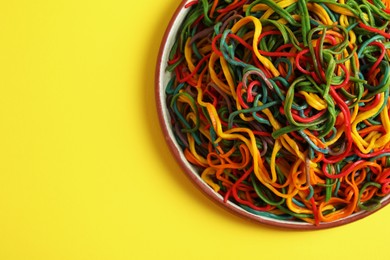 Photo of Plate of spaghetti painted with different food colorings on yellow background, top view. Space for text