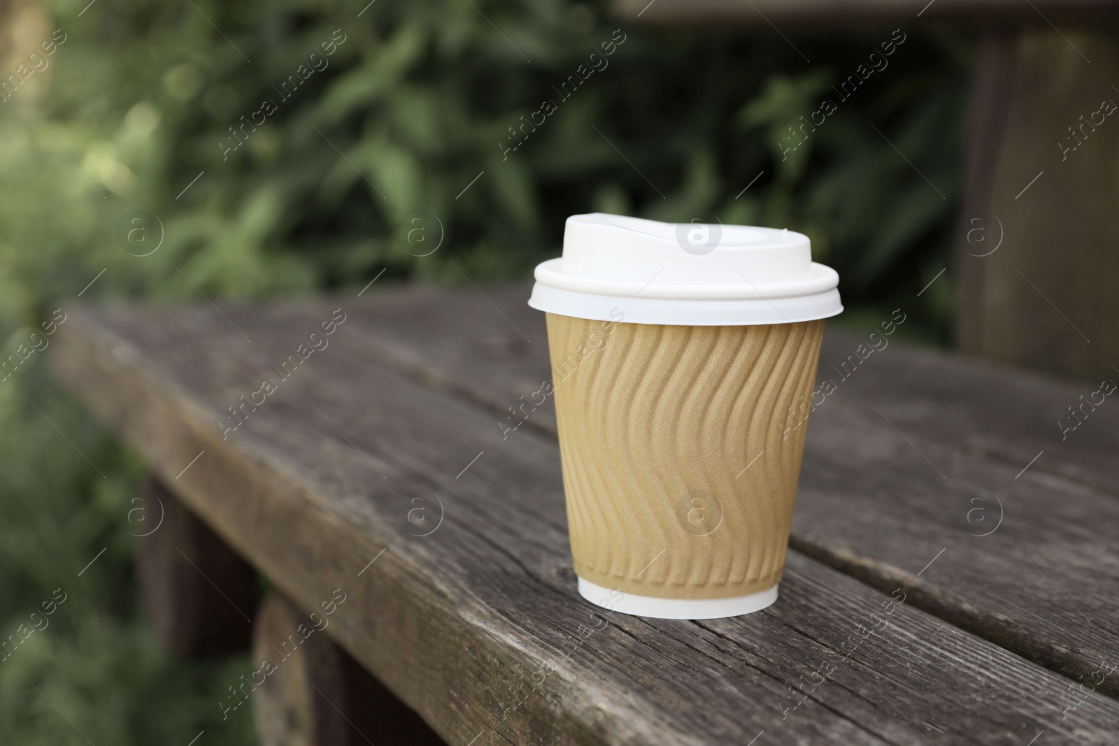 Photo of Paper cup on wooden bench outdoors, space for text. Coffee to go