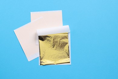 Photo of Edible gold leaf sheets on light blue background, top view. Space for text