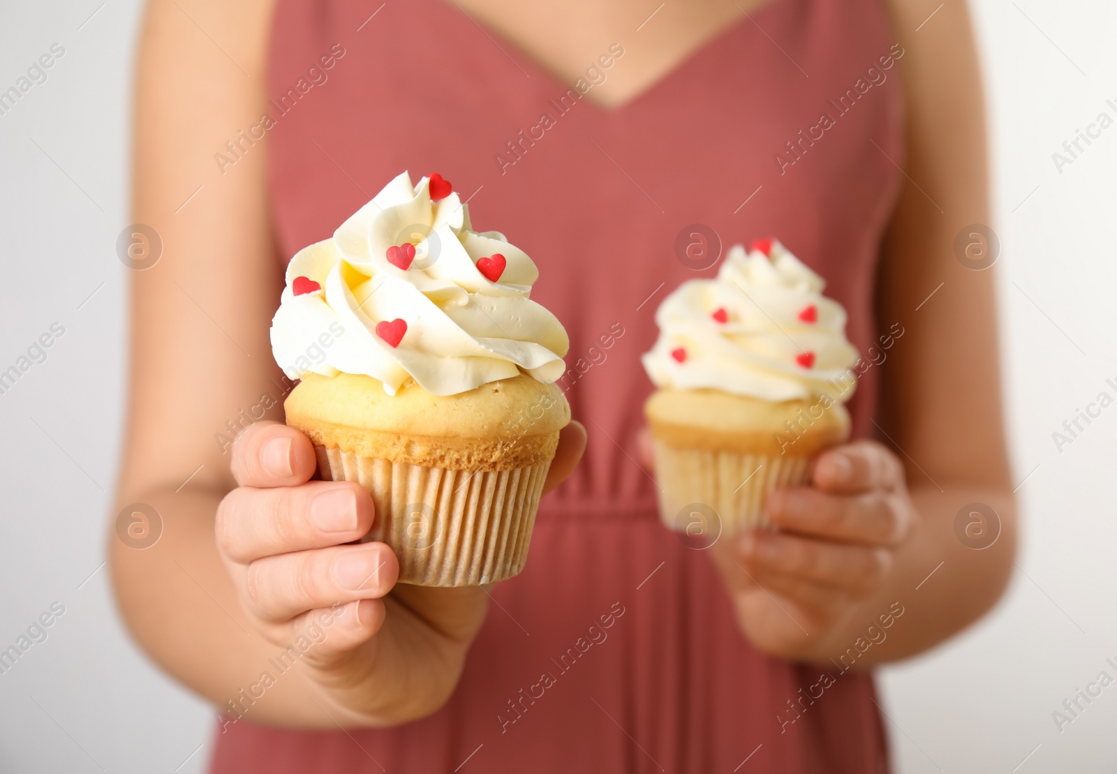 Photo of Woman holding tasty cupcakes for Valentine's Day on light background, closeup