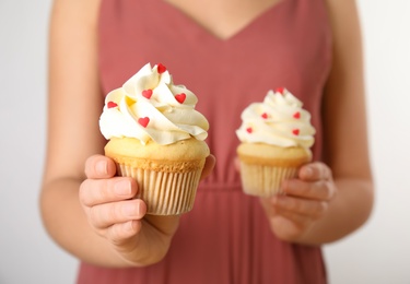 Woman holding tasty cupcakes for Valentine's Day on light background, closeup