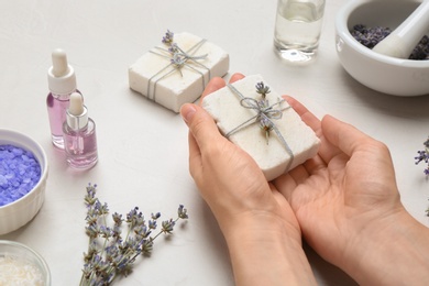 Woman holding hand made soap bar with lavender flowers on light background, closeup