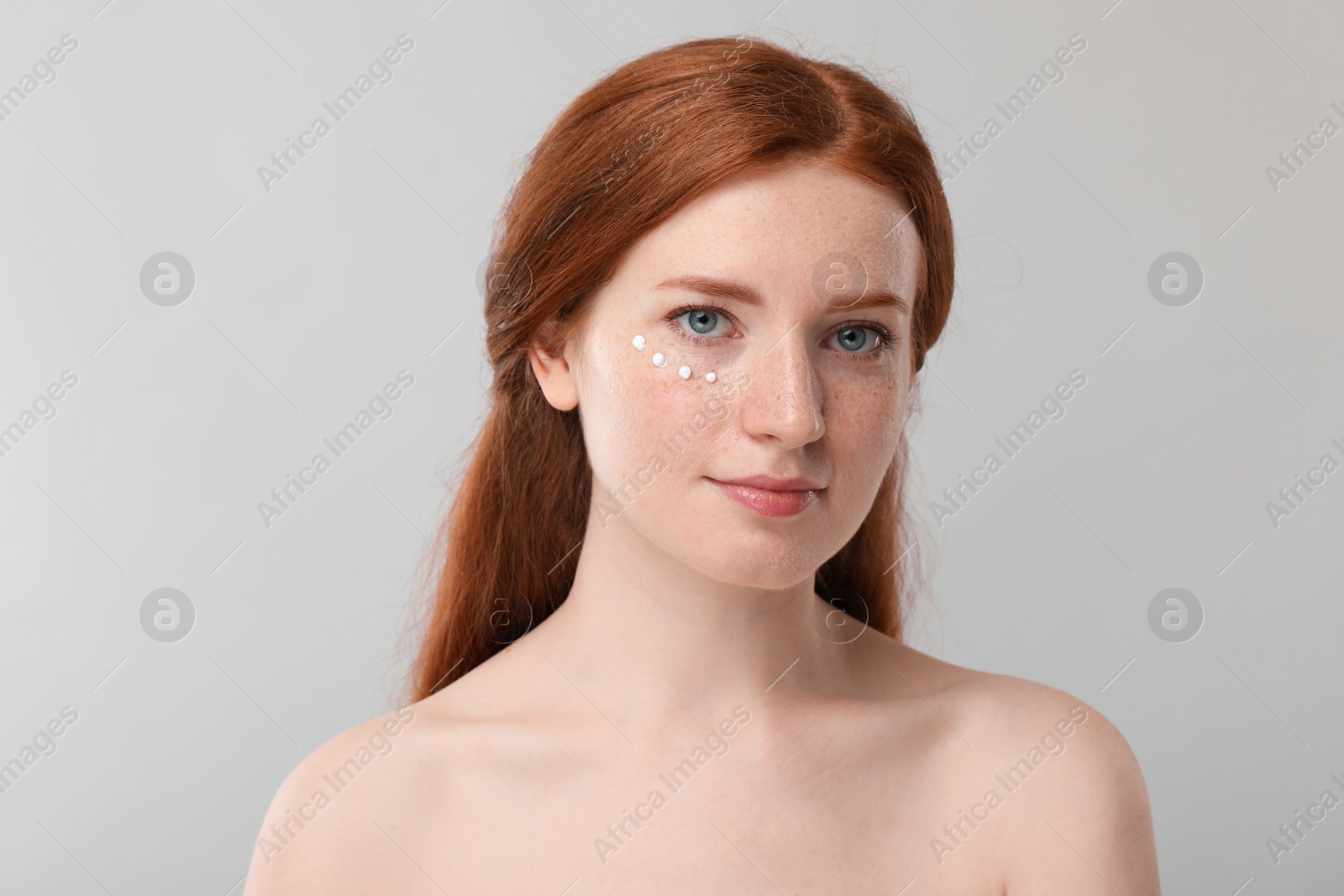 Photo of Beautiful woman with freckles and cream on her face against grey background