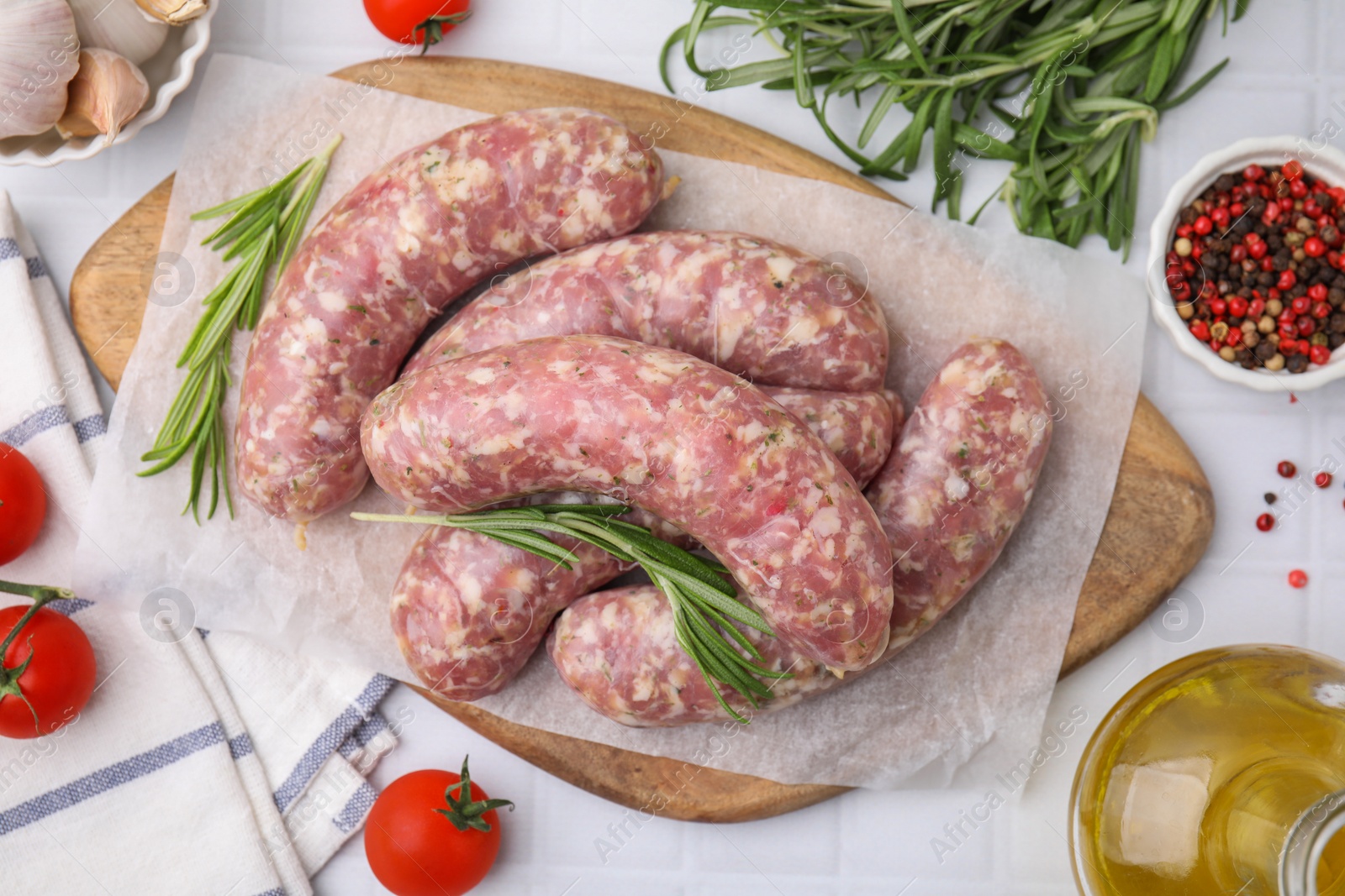 Photo of Raw homemade sausages and different products on white tiled table, flat lay