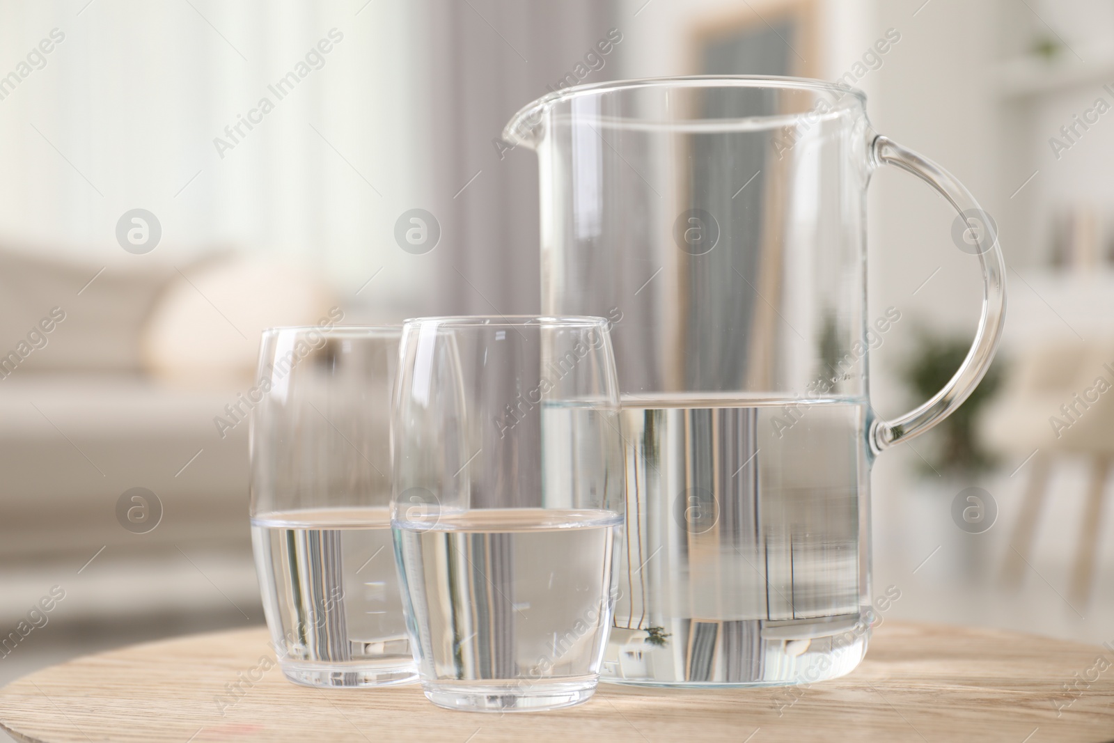 Photo of Jug and glasses with clear water on wooden table indoors, closeup