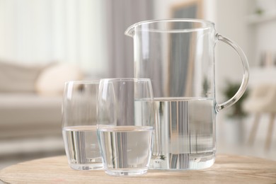 Photo of Jug and glasses with clear water on wooden table indoors, closeup