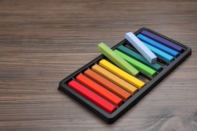 Photo of Colorful pastels in tray on wooden table, space for text. Drawing materials