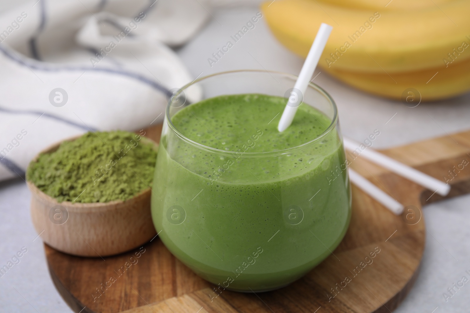 Photo of Glass of tasty matcha smoothie and powder on light table, closeup