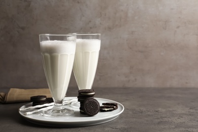 Glasses of milk with chocolate cookies on table against grey background, space for text