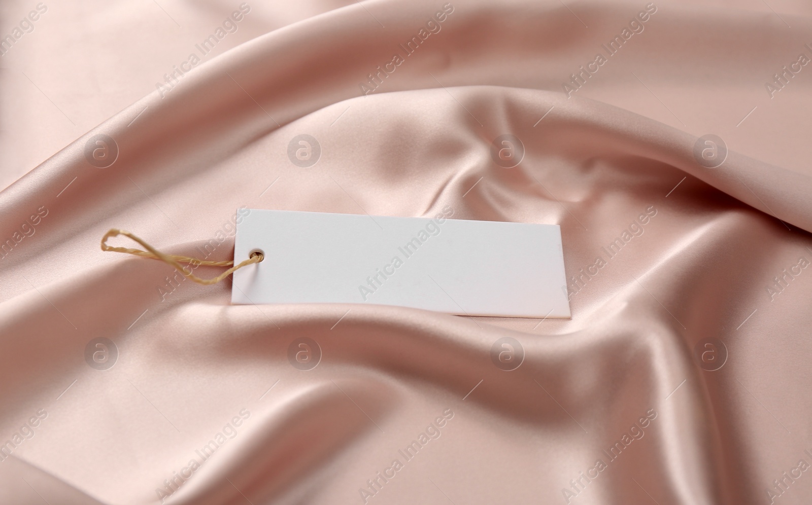 Photo of Blank white tag on pink silky fabric. Space or text