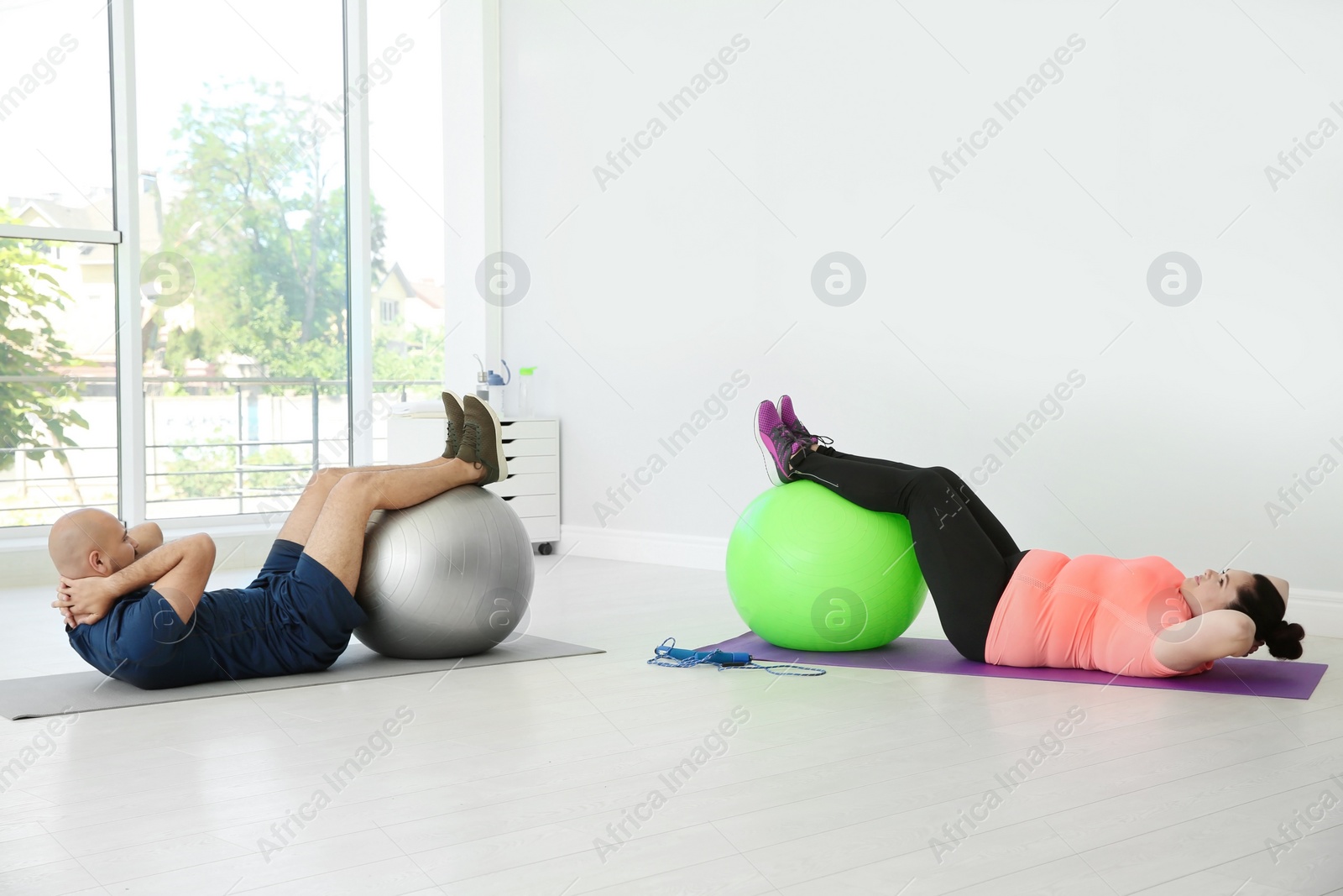 Photo of Overweight man and woman doing exercise with fitness balls in gym