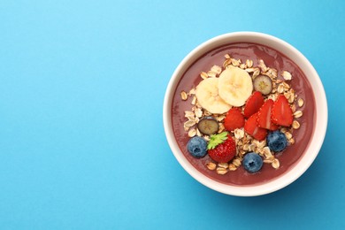 Photo of Delicious smoothie bowl with fresh berries, banana and granola on light blue background, top view. Space for text