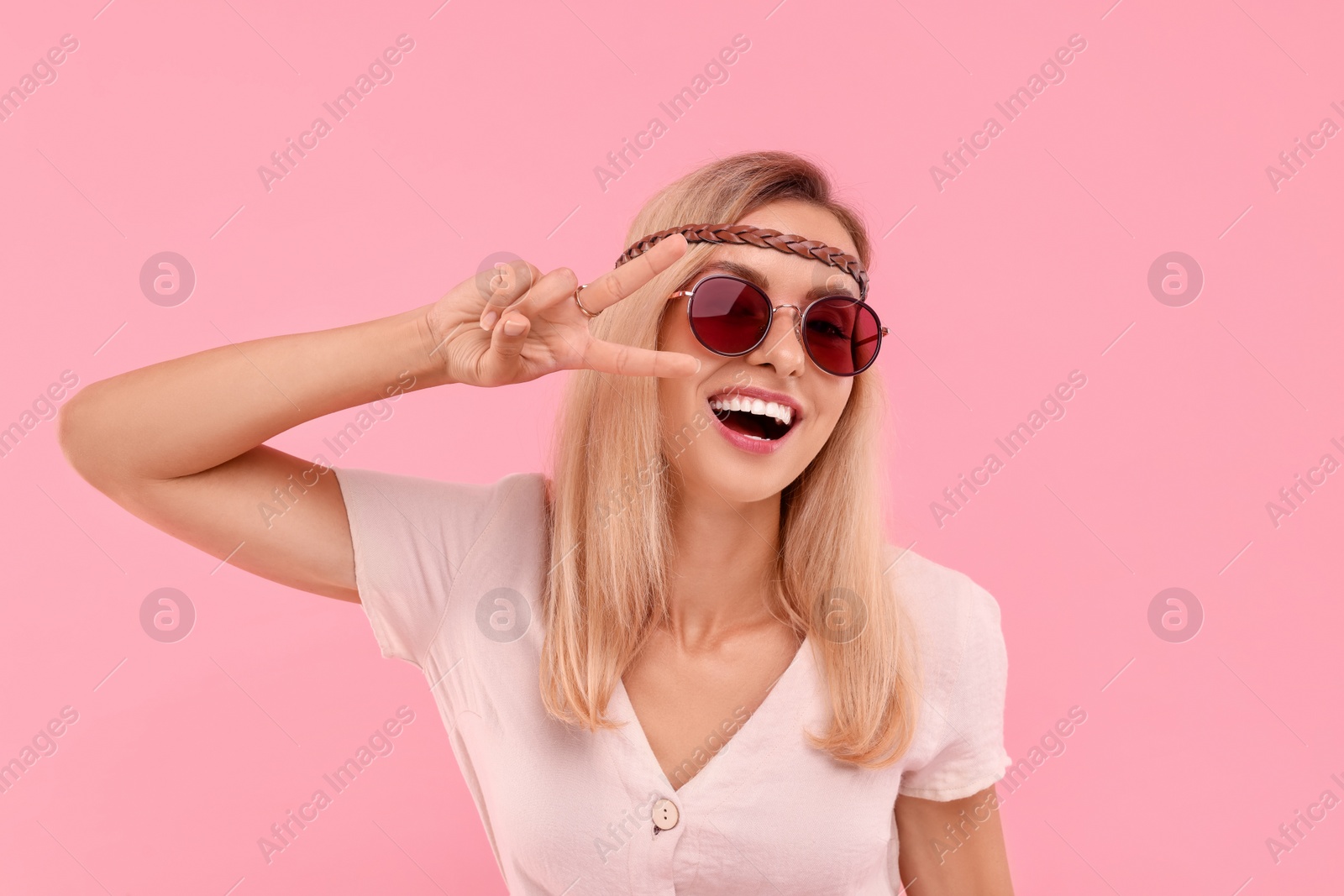 Photo of Portrait of smiling hippie woman showing peace sign on pink background