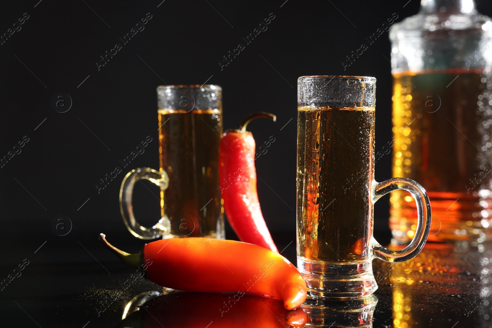 Photo of Red hot chili peppers and vodka on black table