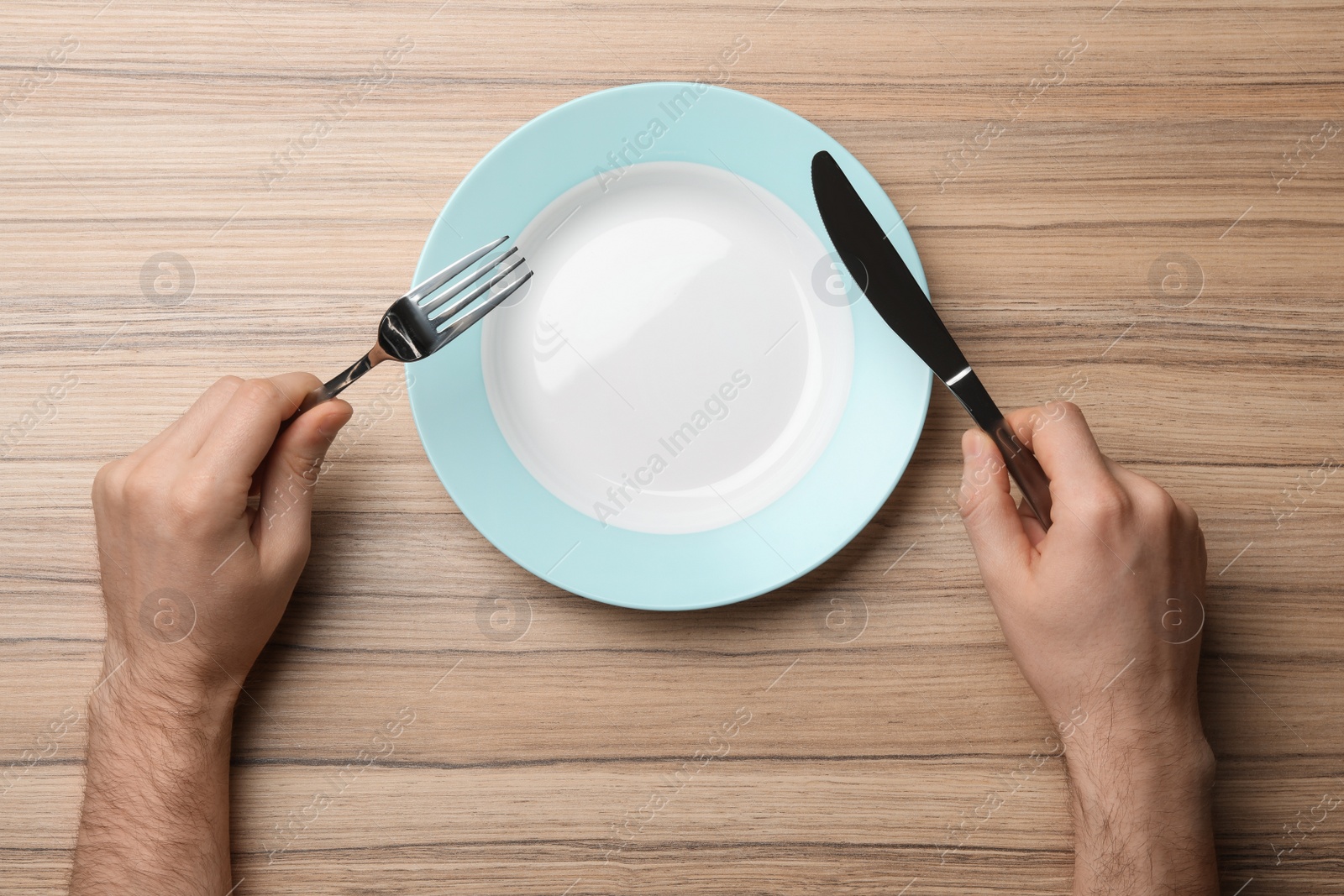 Photo of Man with empty plate and cutlery at wooden table, top view