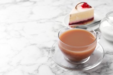 Photo of Delicious tea with milk in glass cup near dessert on white marble table. Space for text