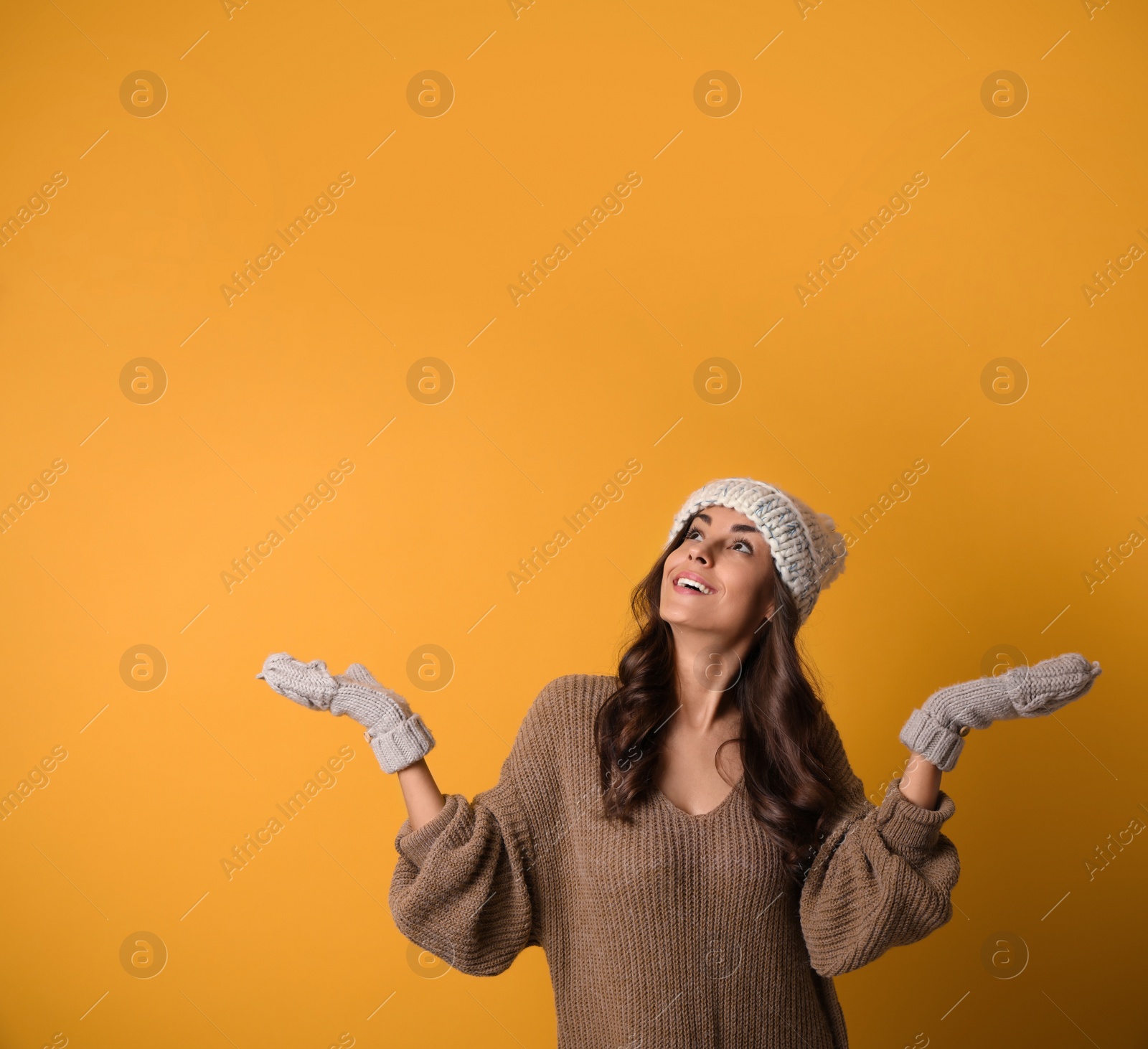 Photo of Young woman in warm sweater, hat and mittens on yellow background. Christmas season