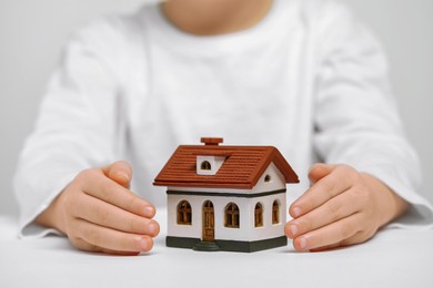 Photo of Home security concept. Little child with house model at white table, closeup