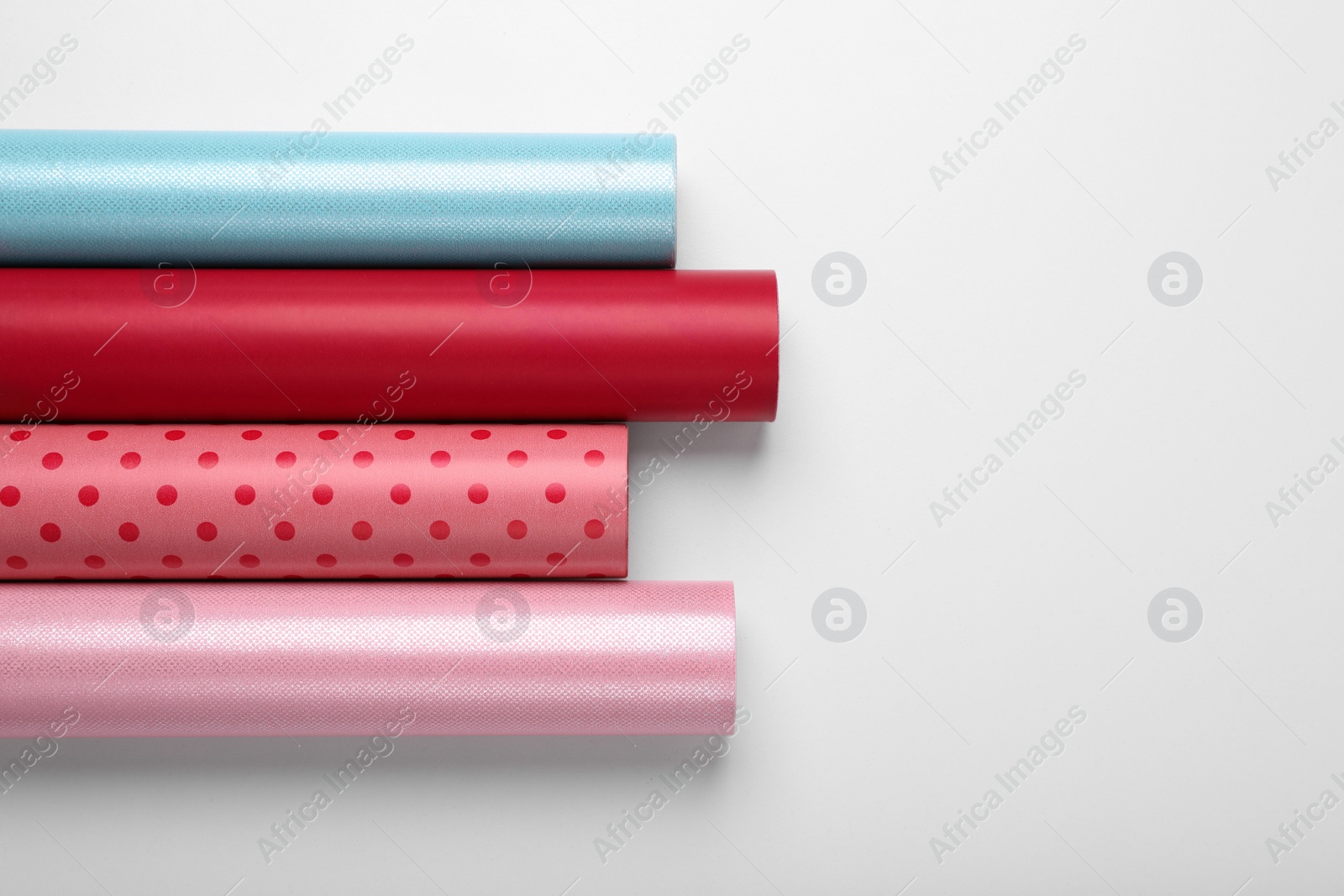 Photo of Rolls of colorful wrapping papers on white background, top view. Space for text