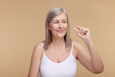 Beautiful woman with vitamin pill on beige background