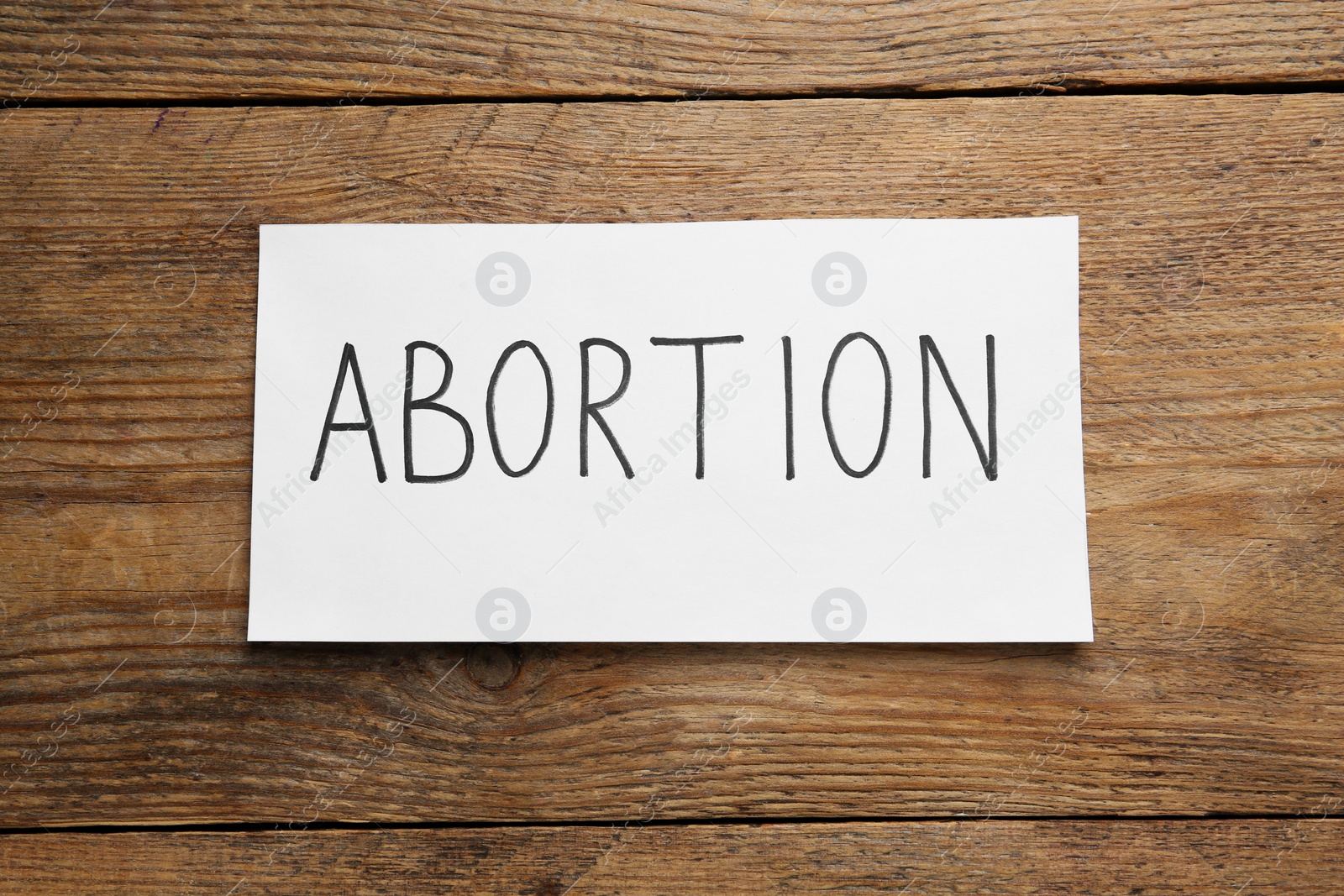 Photo of Paper note with word Abortion on wooden background, top view