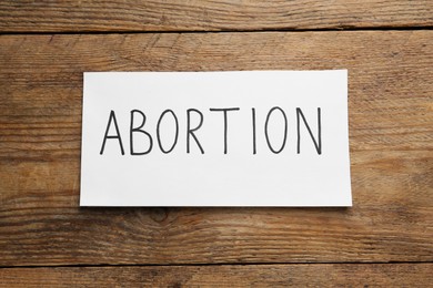 Photo of Paper note with word Abortion on wooden background, top view
