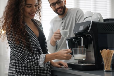 African-American woman talking with colleague while using modern coffee machine in office, closeup