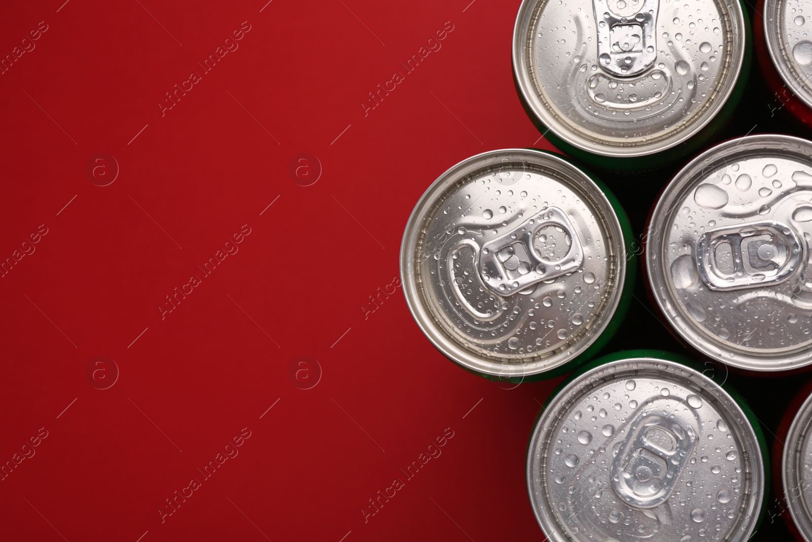 Photo of Energy drinks in wet cans on red background, top view. Space for text