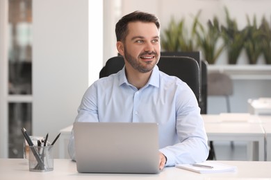 Photo of Happy man using modern laptop at white desk in office