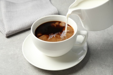 Photo of Pouring milk into cup of hot coffee on grey table