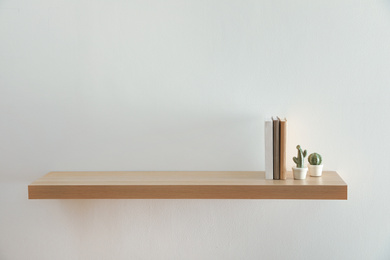 Photo of Wooden shelf with books and decorative cactuses on light wall