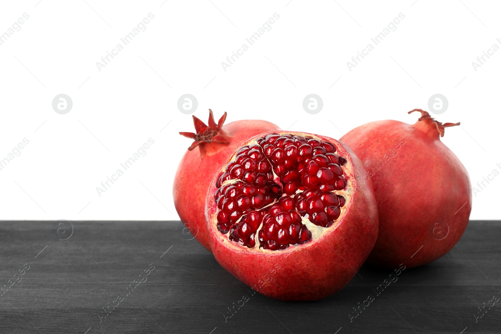 Photo of Fresh pomegranates on black wooden table against white background, space for text