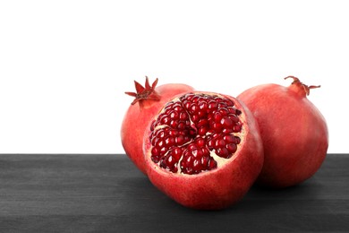 Fresh pomegranates on black wooden table against white background, space for text