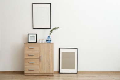 Photo of Wooden cabinet and photo frames in room with white wall, space for text. Interior design